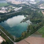 Luftaufnahme eines Ville-Sees mit angrenzendem Gewerbegebiet