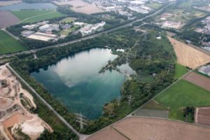 Luftaufnahme eines Ville-Sees mit angrenzendem Gewerbegebiet